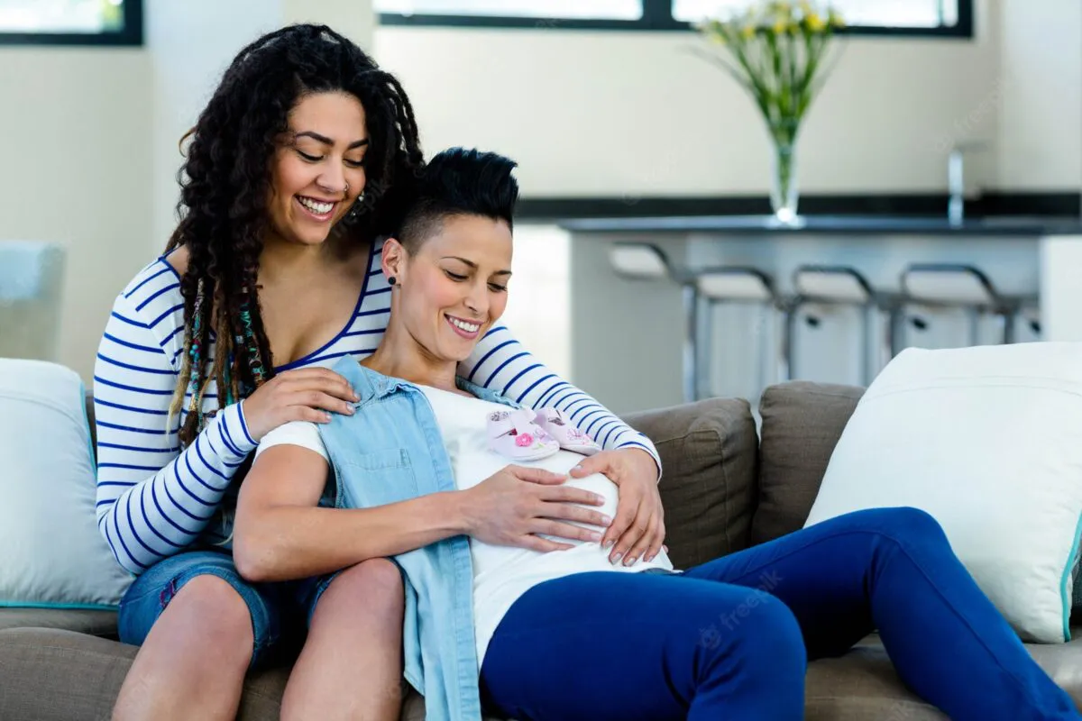 pareja-lesbianas-embarazadas-sentada-sofa-par-zapatos-bebe-rosa_107420-13364-1200x800